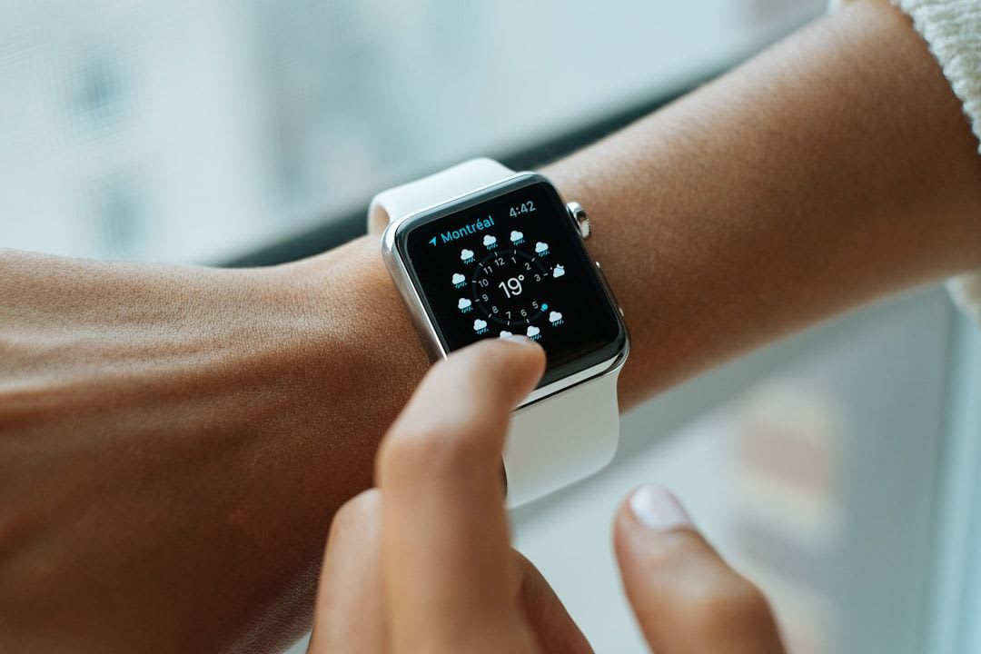 Person bedient eine Smartwatch am Handgelenk, im Hintergrund eine geöffnete Smartwatch Bedienungsanleitung Deutsch PDF auf einem Laptop. | Foto: Luke Chesser