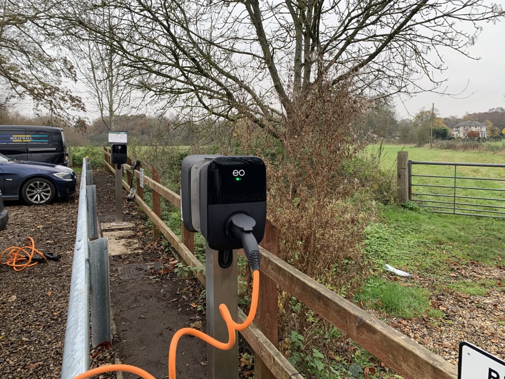 An EO Genius 2 charger with green LED active on a metal pedestal in Hollywell's office car park in St Albans.