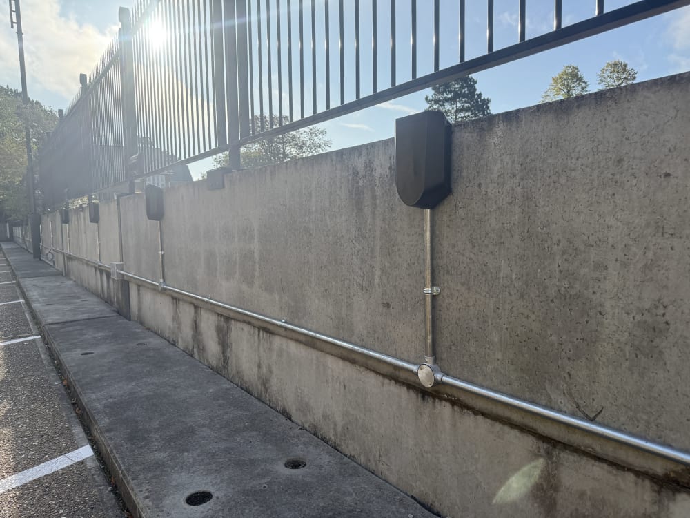 Steel galvanised conduit routing below Easee charger backplates on the concrete perimeter wall at Hampton.