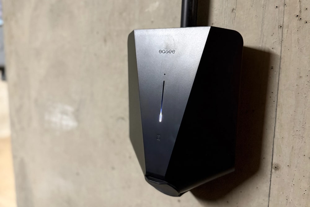 Close up of a black Easee smart charger mounted on a bare concrete wall in the underground car park at Portland Court, status light lit.