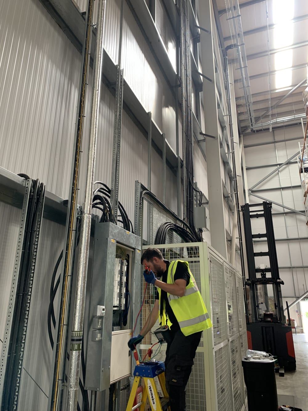 Electrician routing SWA cables through overhead cable tray inside the Zeus Packaging warehouse, Biggleswade.
