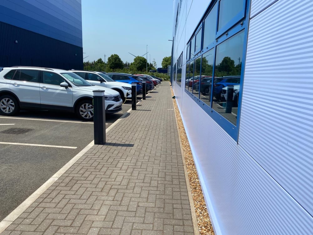 A business park car park lined with protective bollards and marked bays, a typical commercial EV charging site in the UK.