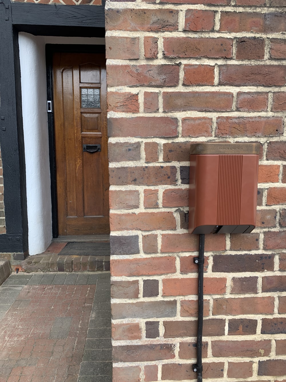 A weatherproof enclosure housing EV charging equipment, fitted to the brick wall of a period property in the UK.
