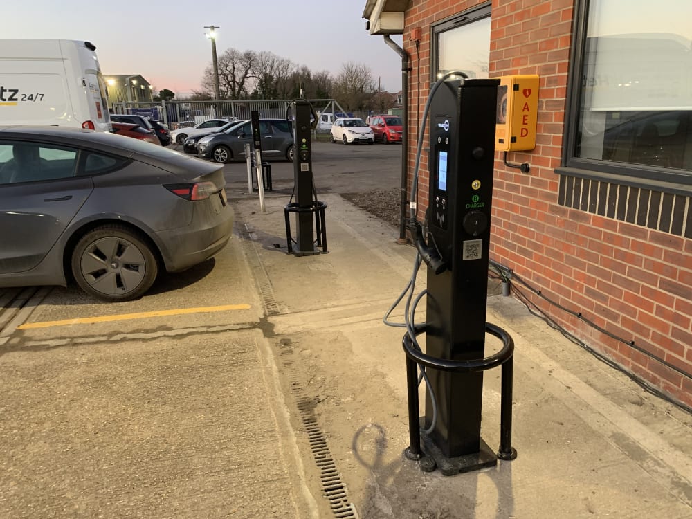 Two freestanding pedestal EV chargers installed in a commercial car park beside an office building in the UK.