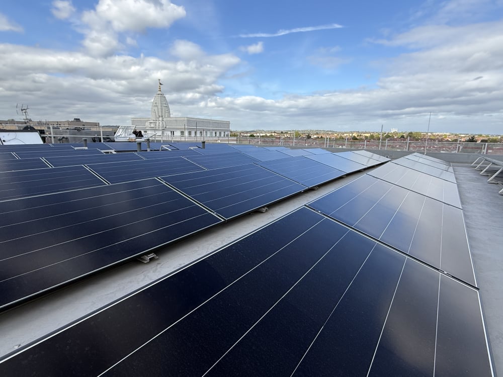 Ballasted black framed solar panels across a flat commercial rooftop at Alpine Place, Colindale, with Neasden temple on the London horizon