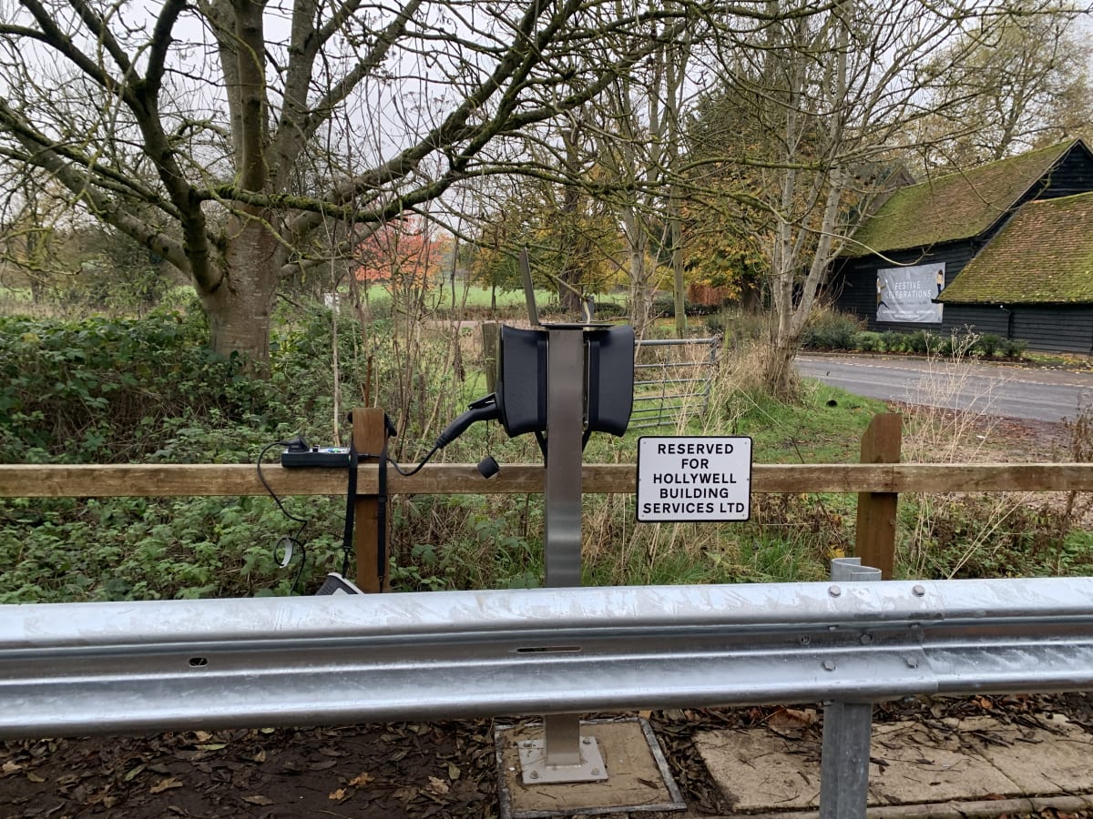 A dual EO Genius 2 charging pedestal with crash barrier and reserved bay sign at Hollywell's fleet depot in St Albans.