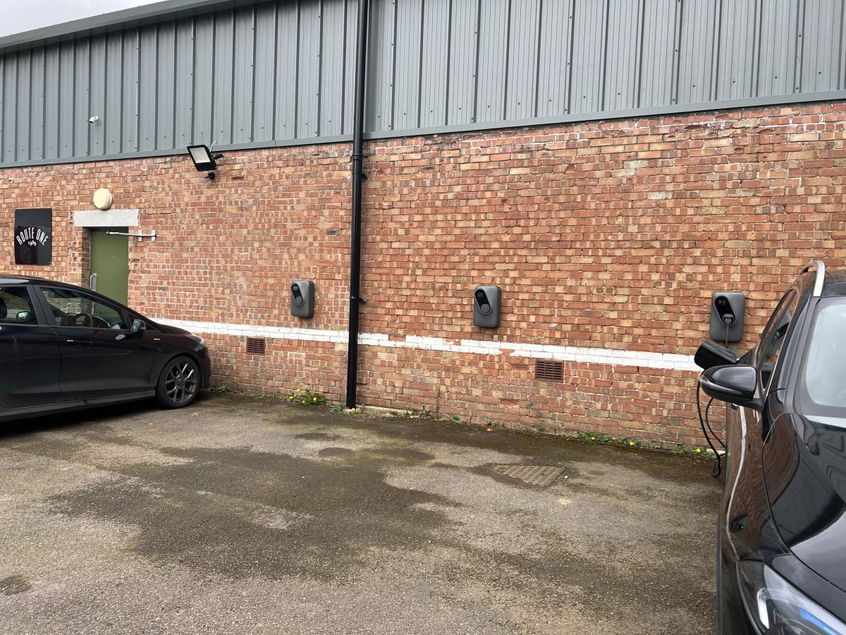 Three EV chargers installed on the brick wall near the Route One warehouse entrance at Acton Turville