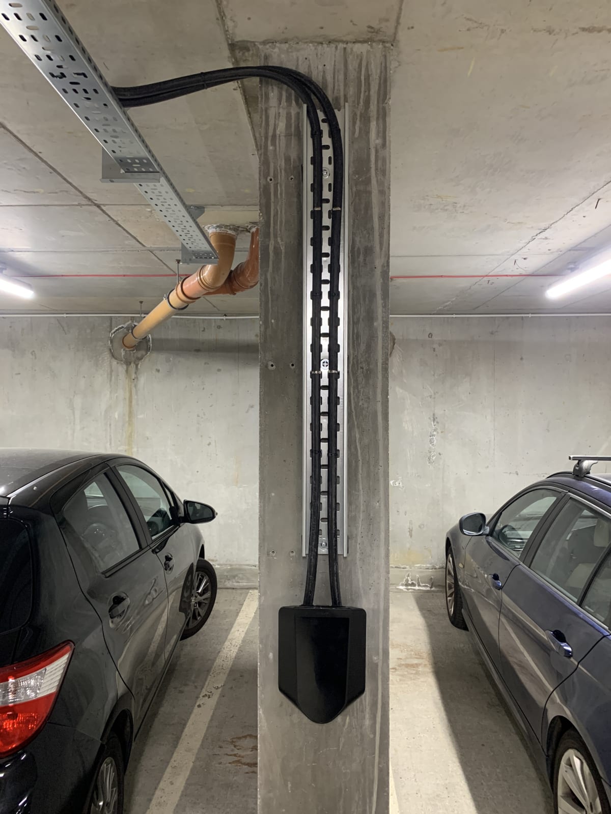 Easee charger installed on a pillar with armoured cable dropping from cable tray in an apartment car park in Hendon