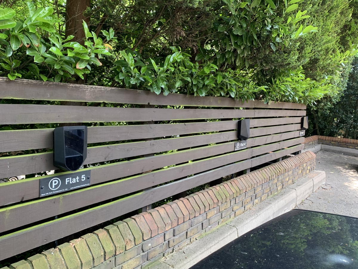 Two Easee One EV chargers on wooden fencing with hidden cable containment behind dense greenery at Hill Court, Highgate