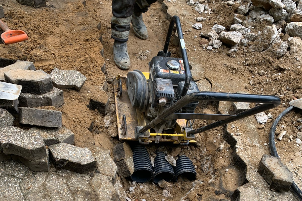 A plate compactor preparing the trench through Z-block paving during EV charging groundworks at Hill Court, Highgate