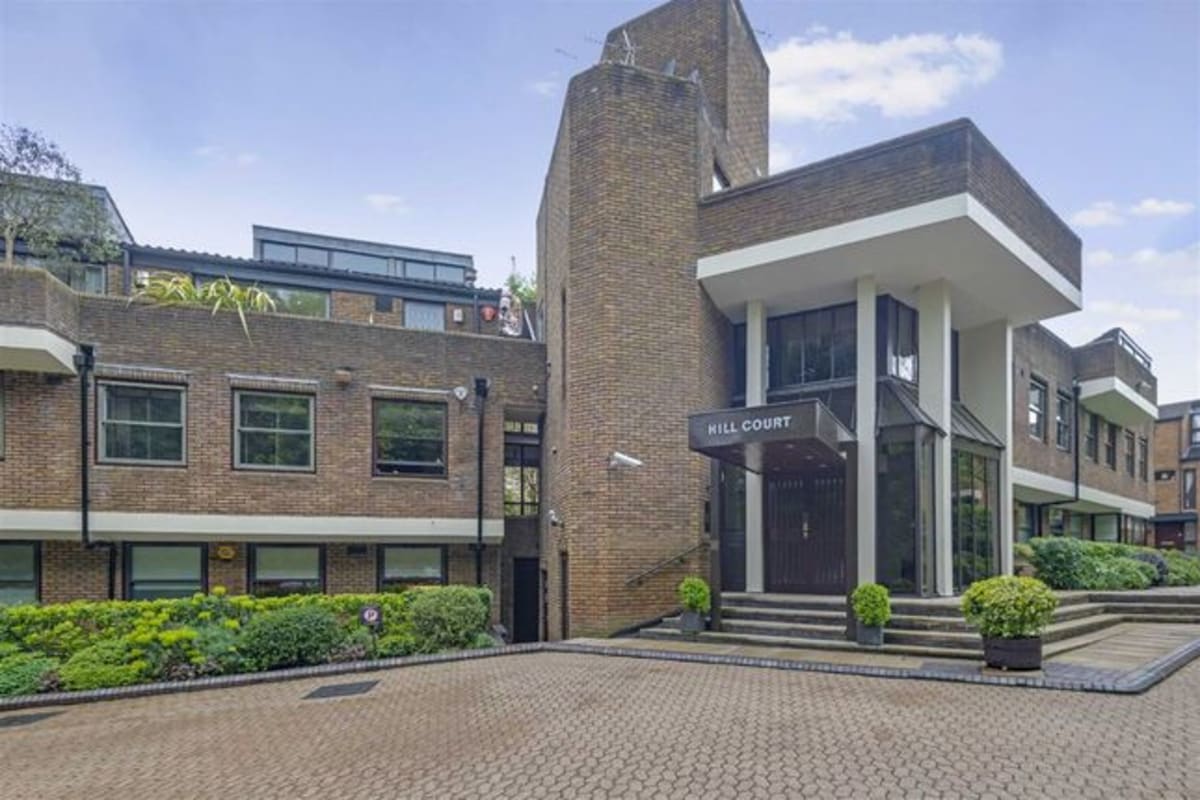 The main entrance of Hill Court residential apartments showing the building name sign and landscaped forecourt in Highgate, London