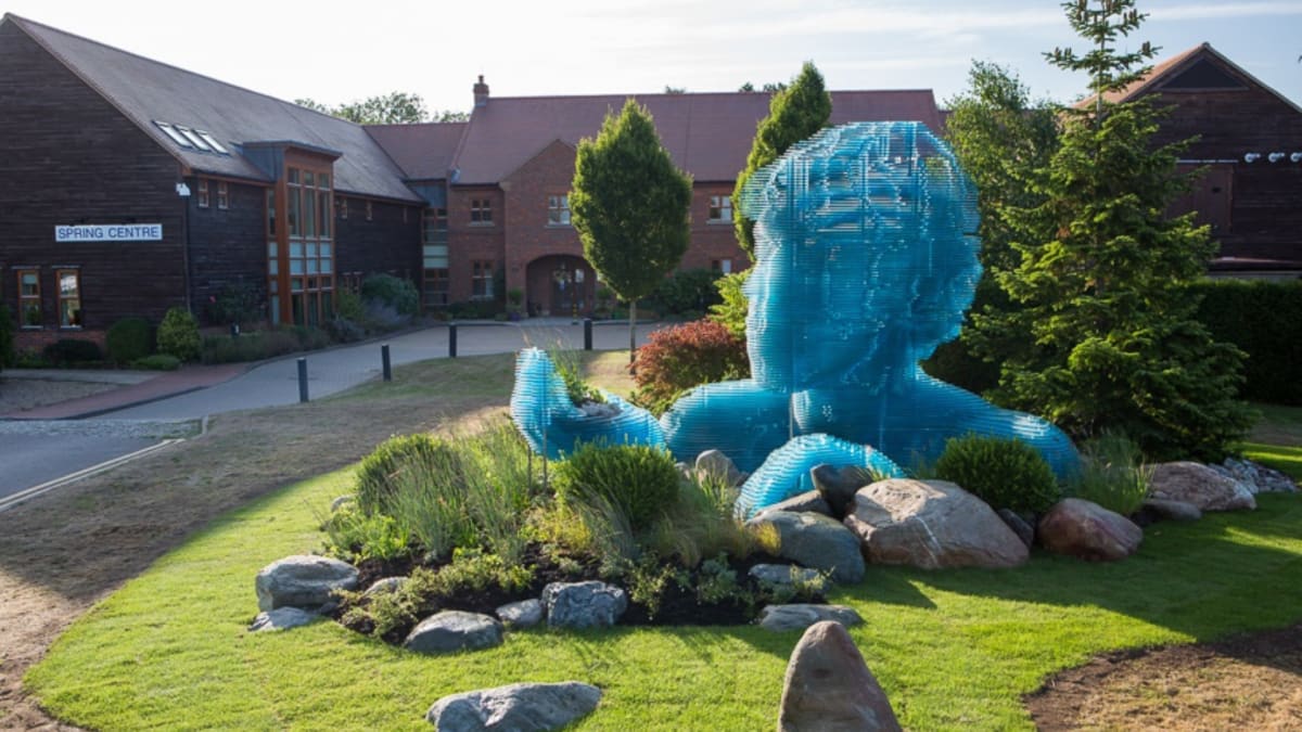 Main entrance of The Hospice of St Francis in Berkhamsted featuring blue sculpture of a human head with open hand in landscaped gardens