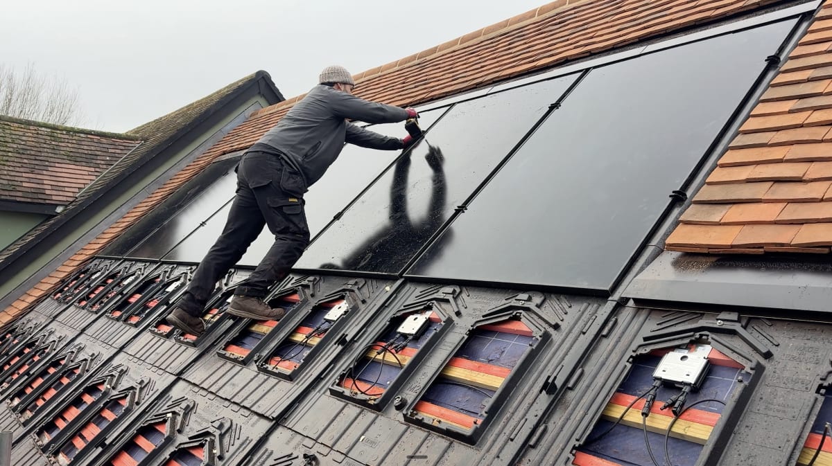 EV-ON engineer cleaning a newly installed in-roof solar panel on a clay tile cottage roof in Broxted, Essex, with GSE trays visible below.