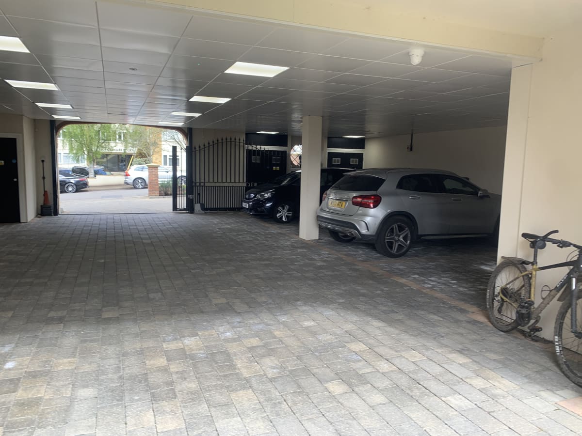 The gated entrance to a covered residential car park with block paving at an apartment development in Hendon