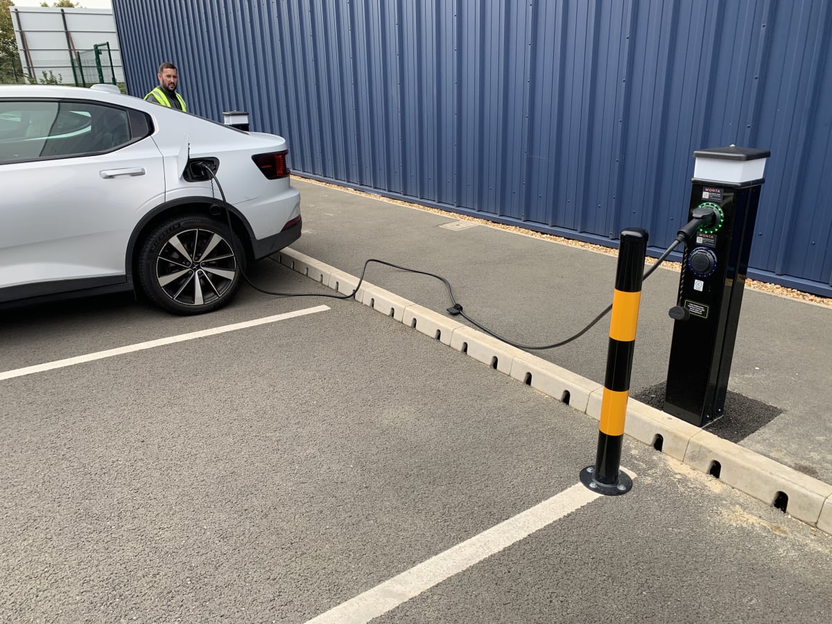 White electric vehicle charging at a Rolec pedestal charger with protective bollard at Zeus Packaging, Biggleswade