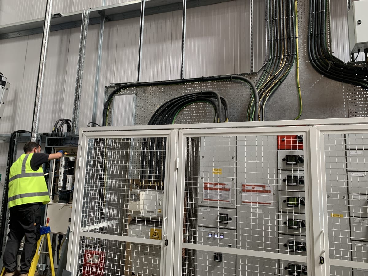 Electrician connecting EV charging circuits at the main distribution board inside Zeus Packaging facility, Biggleswade