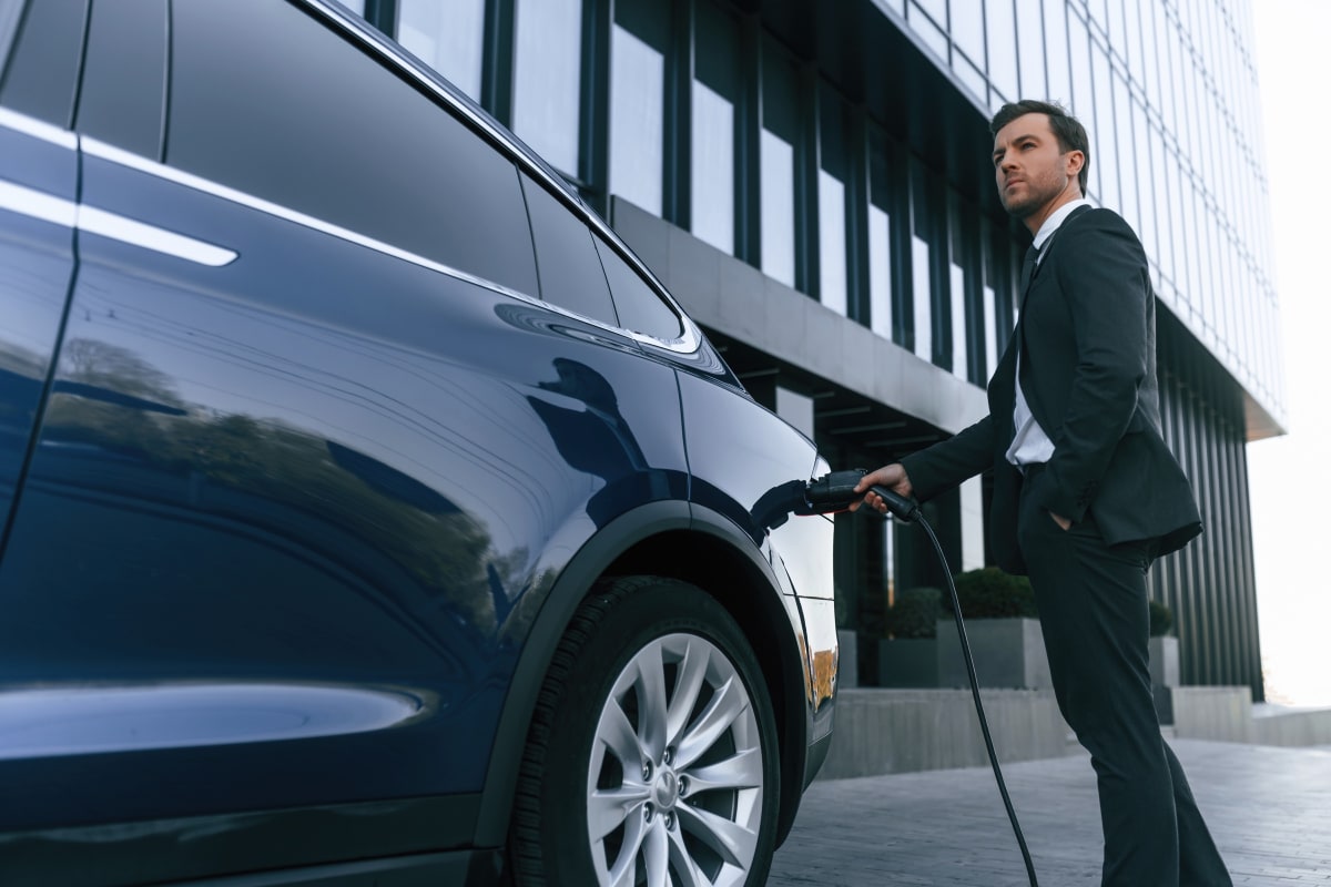 A business professional charging a dark electric car outside a modern glass office building