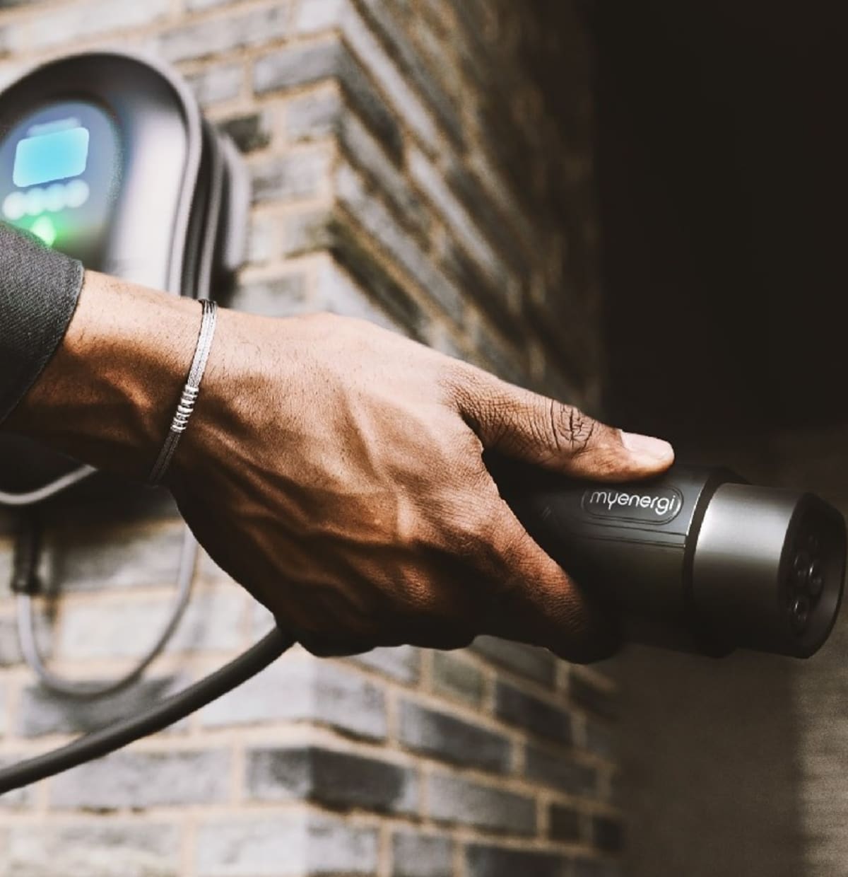 A Zappi home EV charger with its cable and plug on a brick wall