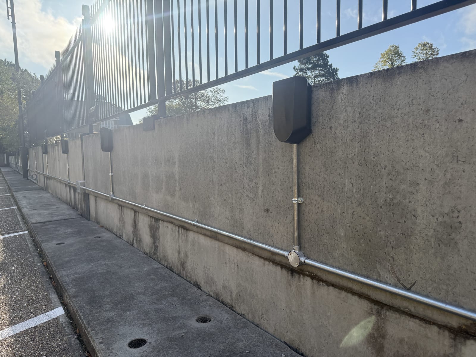 Steel galvanised conduit routing below Easee charger backplates on the concrete perimeter wall at Hampton.