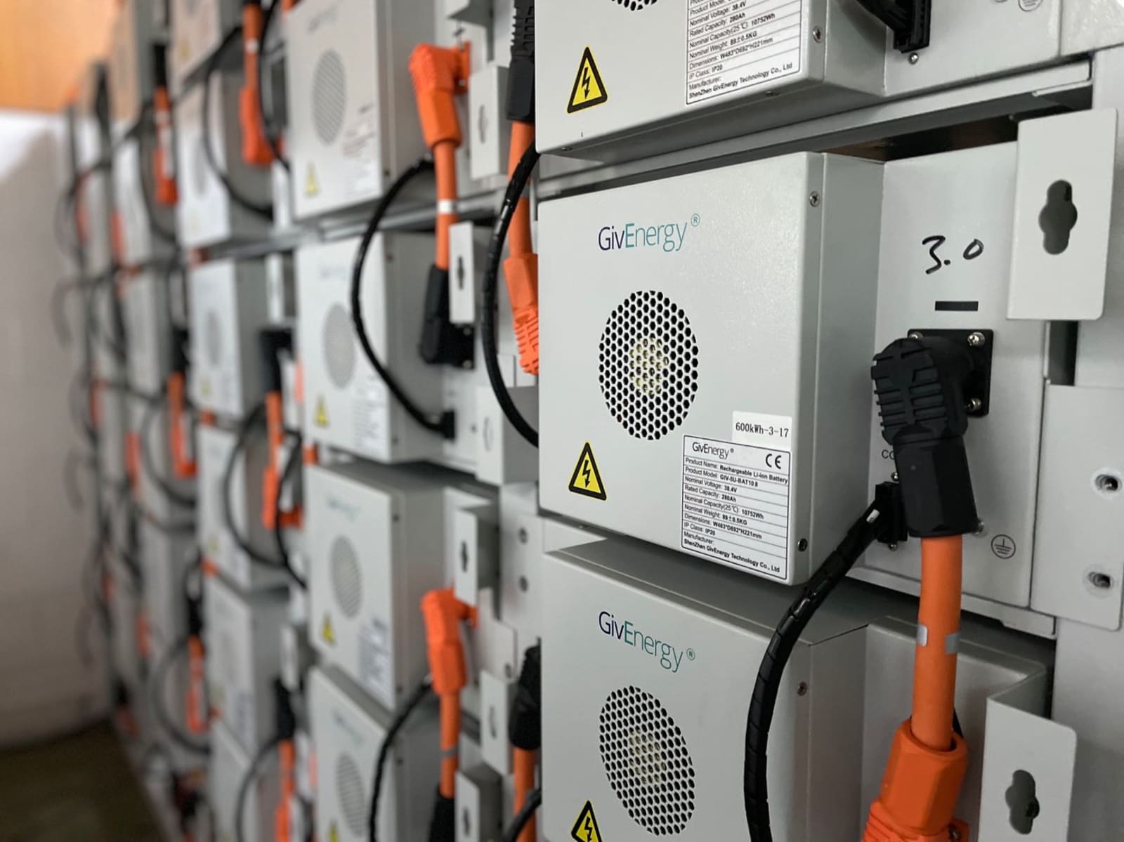 Close-up of stacked GivEnergy high voltage lithium-ion battery modules with orange DC cabling in a commercial storage system.