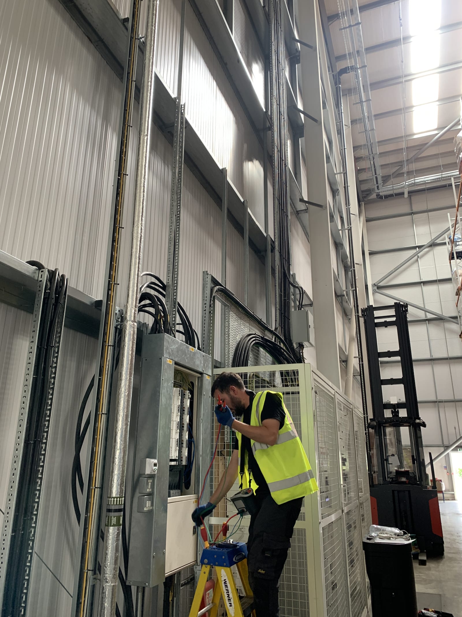 Electrician routing SWA cables through overhead cable tray inside the Zeus Packaging warehouse, Biggleswade.