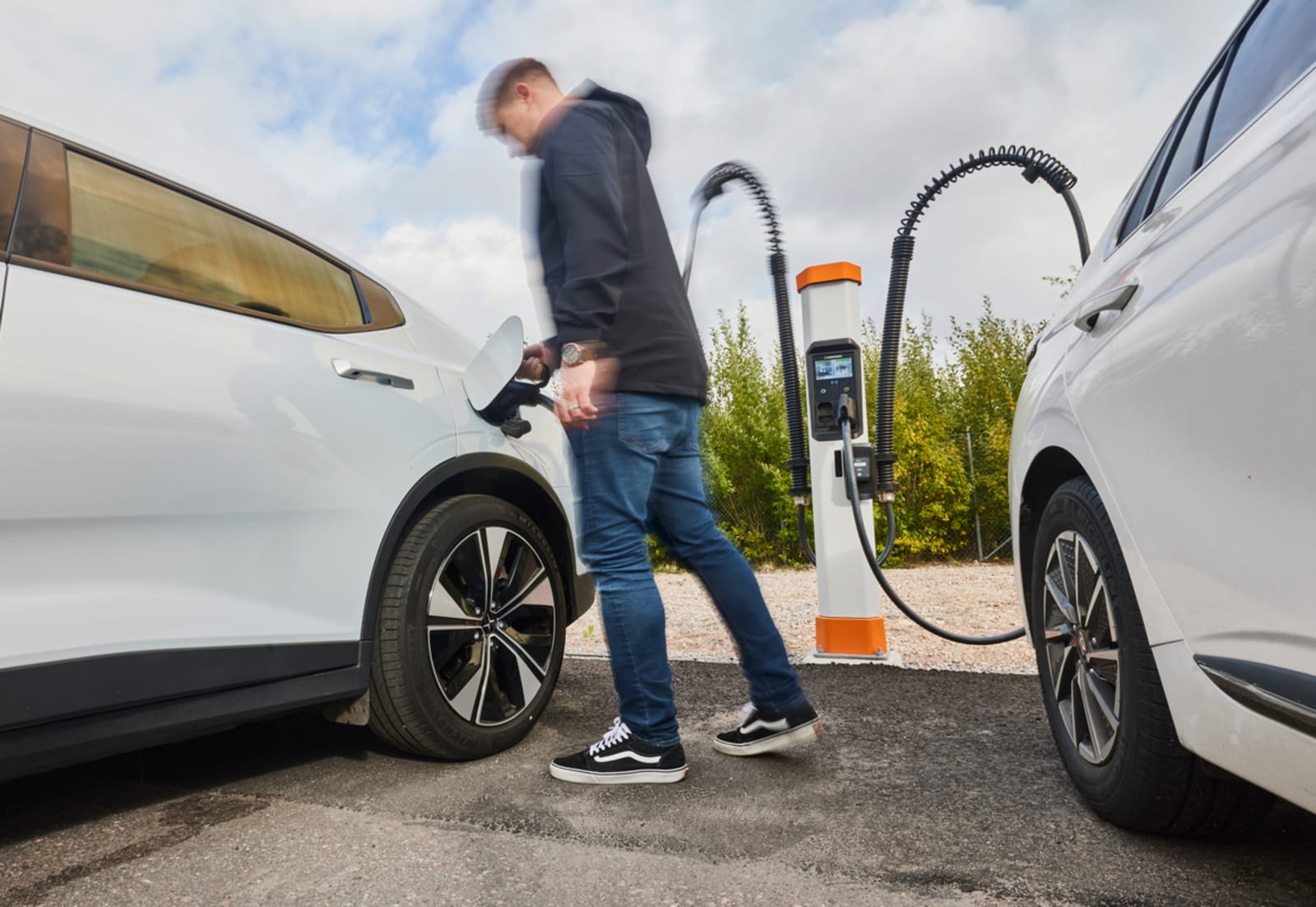 Driver plugging in an electric vehicle between two white cars at a Kempower dual charging point.
