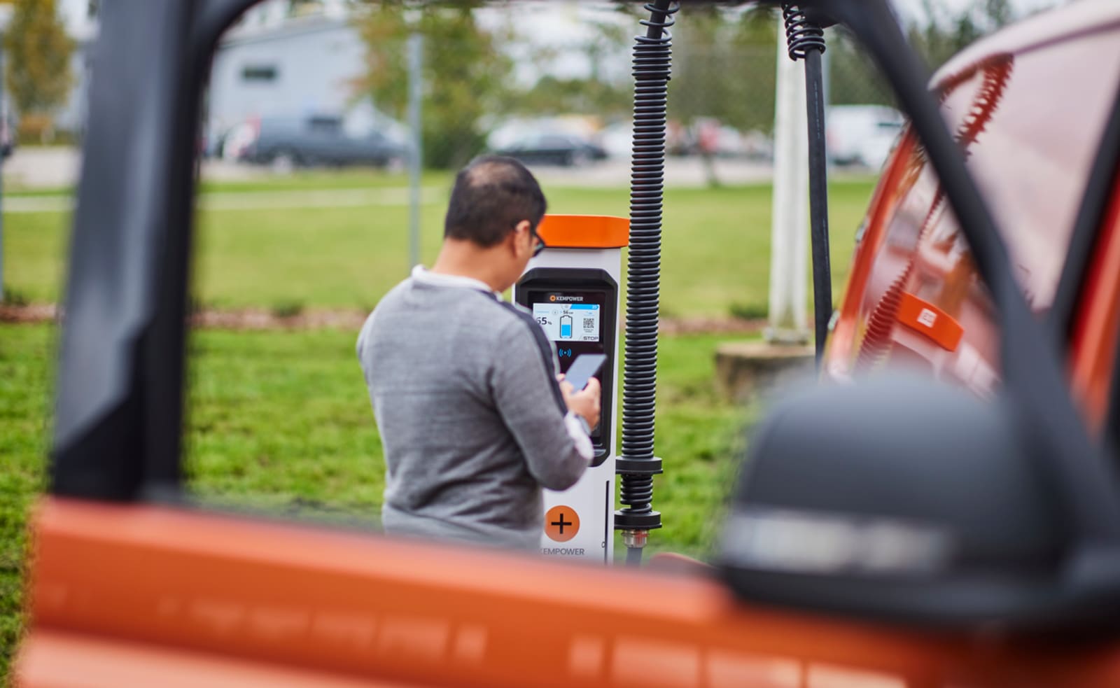 Driver using the touchscreen interface on a Kempower DC fast charger at a commercial charging station.