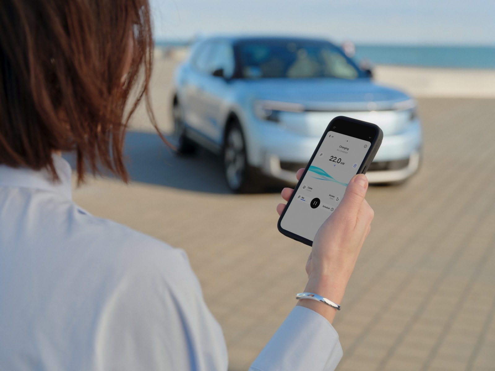 A driver starting an EV charge remotely from the Easee app with their car parked ahead.