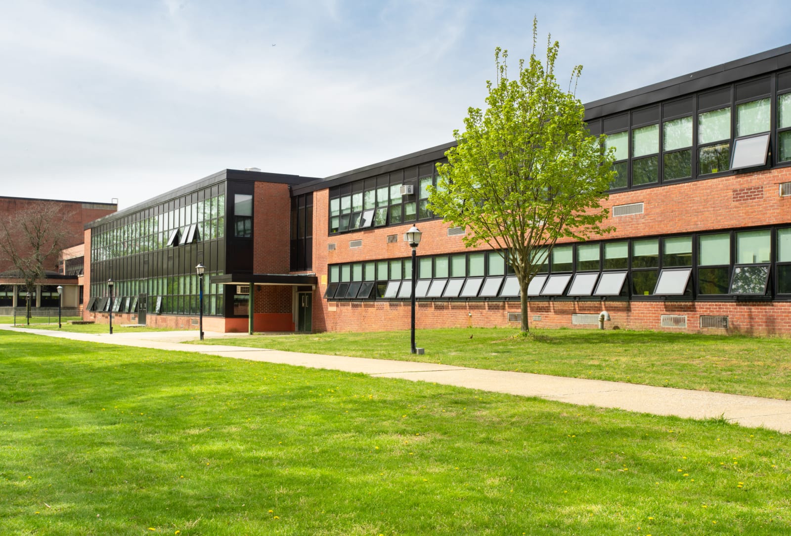 Exterior of a UK school building with brick and glass classrooms, lawn and trees, suited to campus EV charging