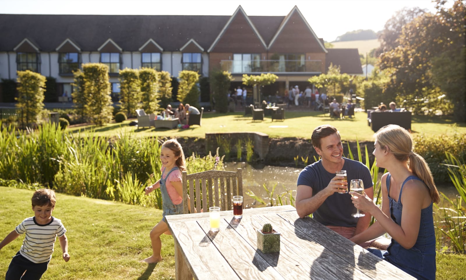 A family enjoying drinks at an outdoor table in the garden of a countryside hotel on a sunny day.