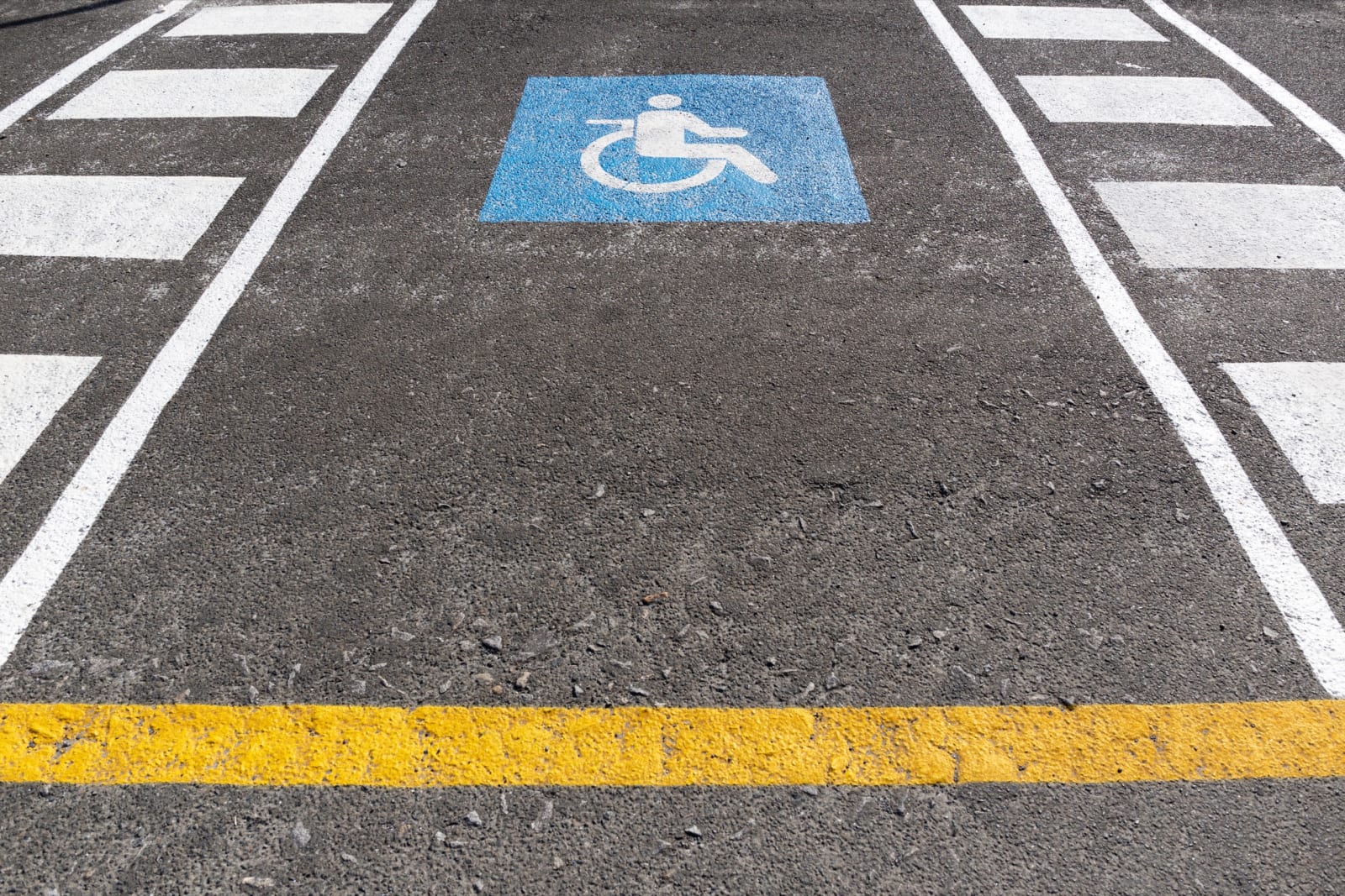 A blue wheelchair accessibility symbol painted in a marked disabled parking bay with hatched access markings.
