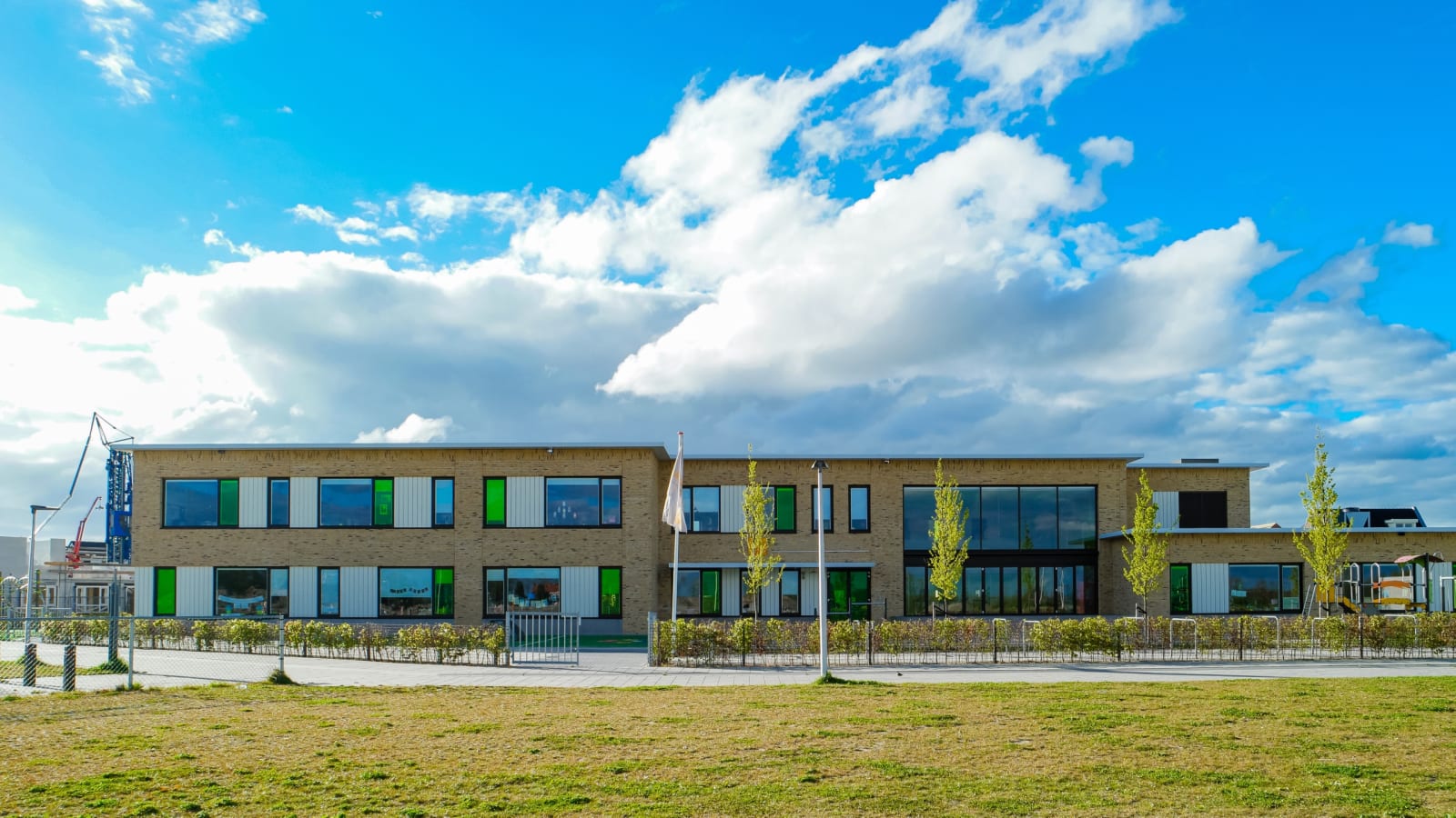 A modern newly built school building with a playground under a bright blue sky.