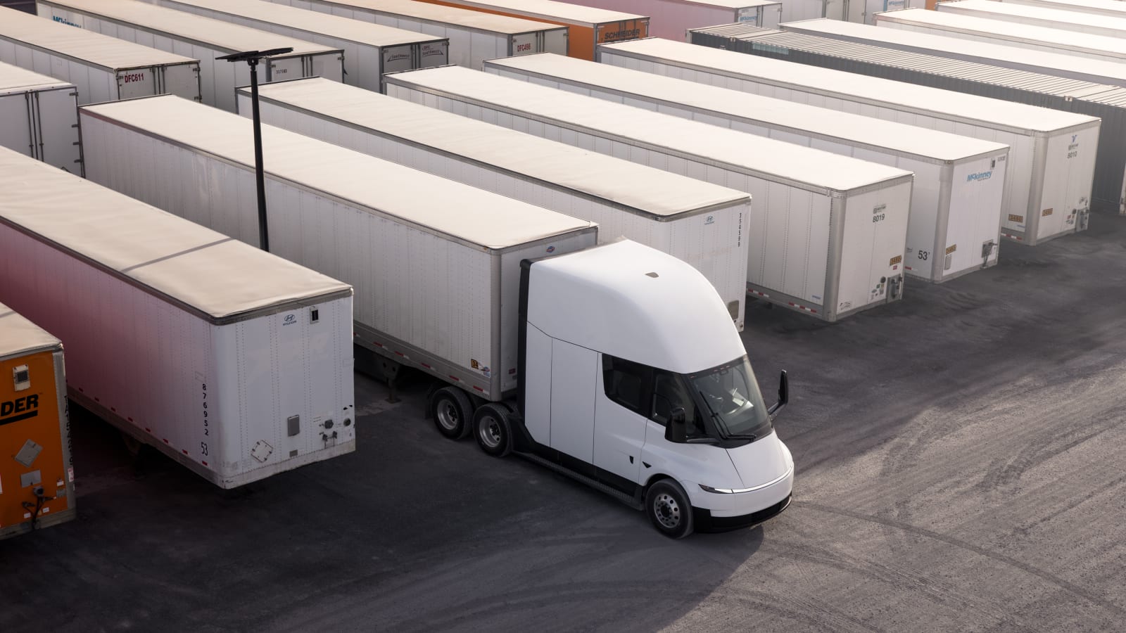 Aerial view of a Tesla Semi electric truck reversing between rows of trailers in a logistics yard.