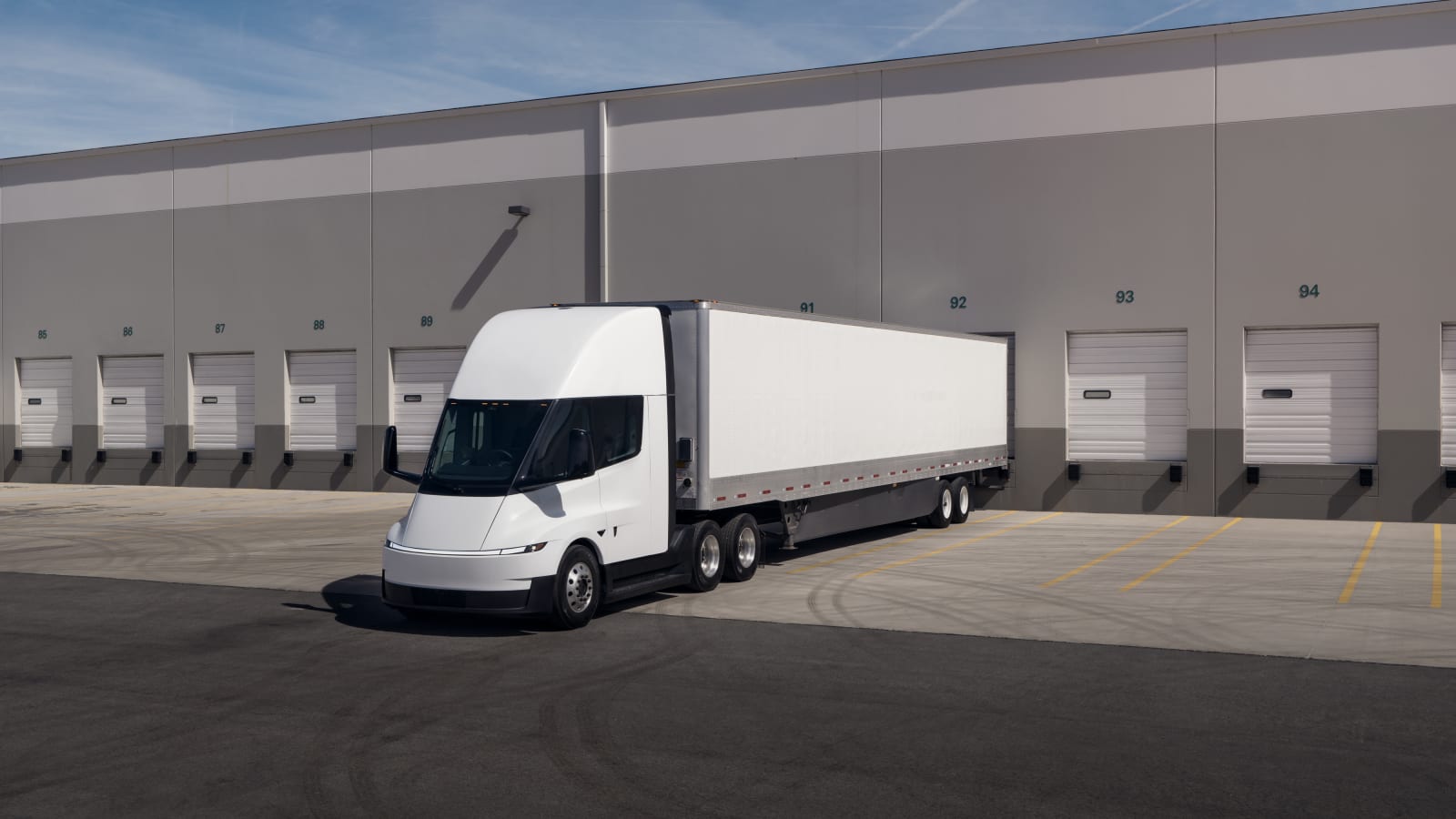 Tesla Semi electric truck parked at a loading dock bay outside a distribution warehouse.