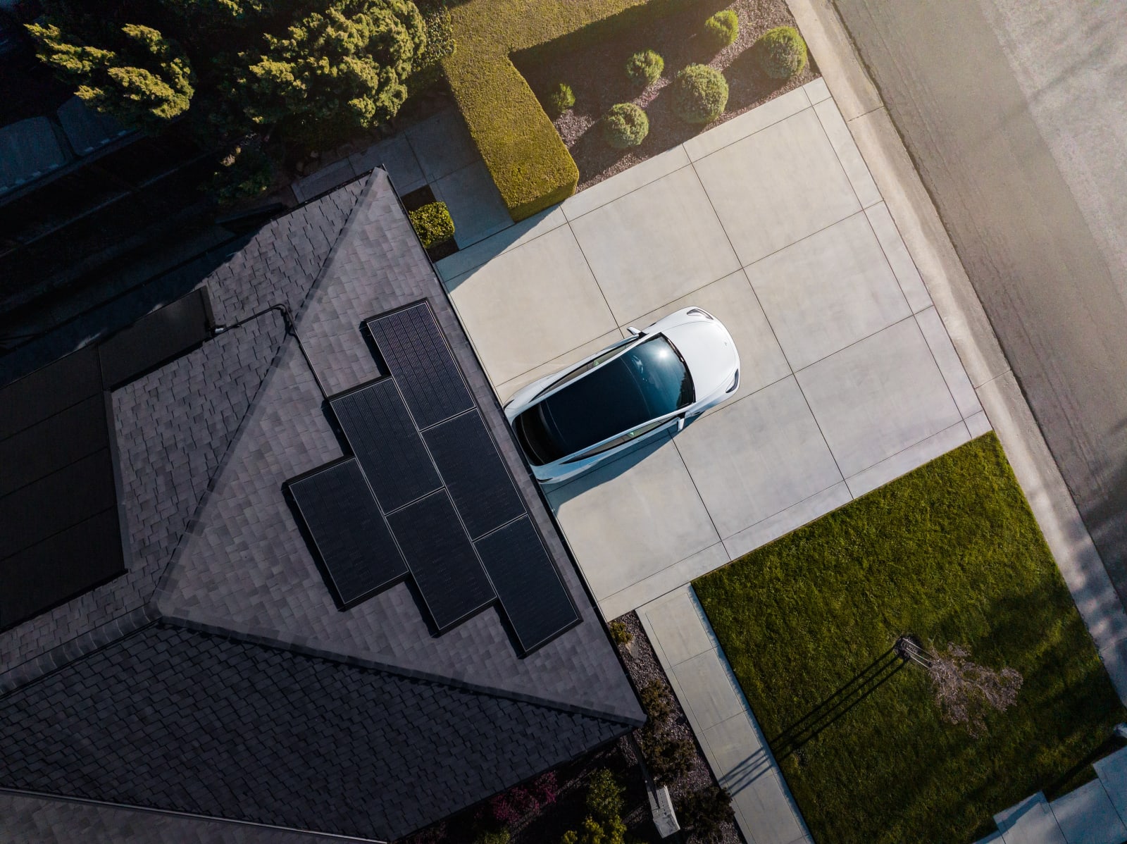 Aerial view of a house roof fitted with Tesla solar panels beside a driveway with a car parked outside.