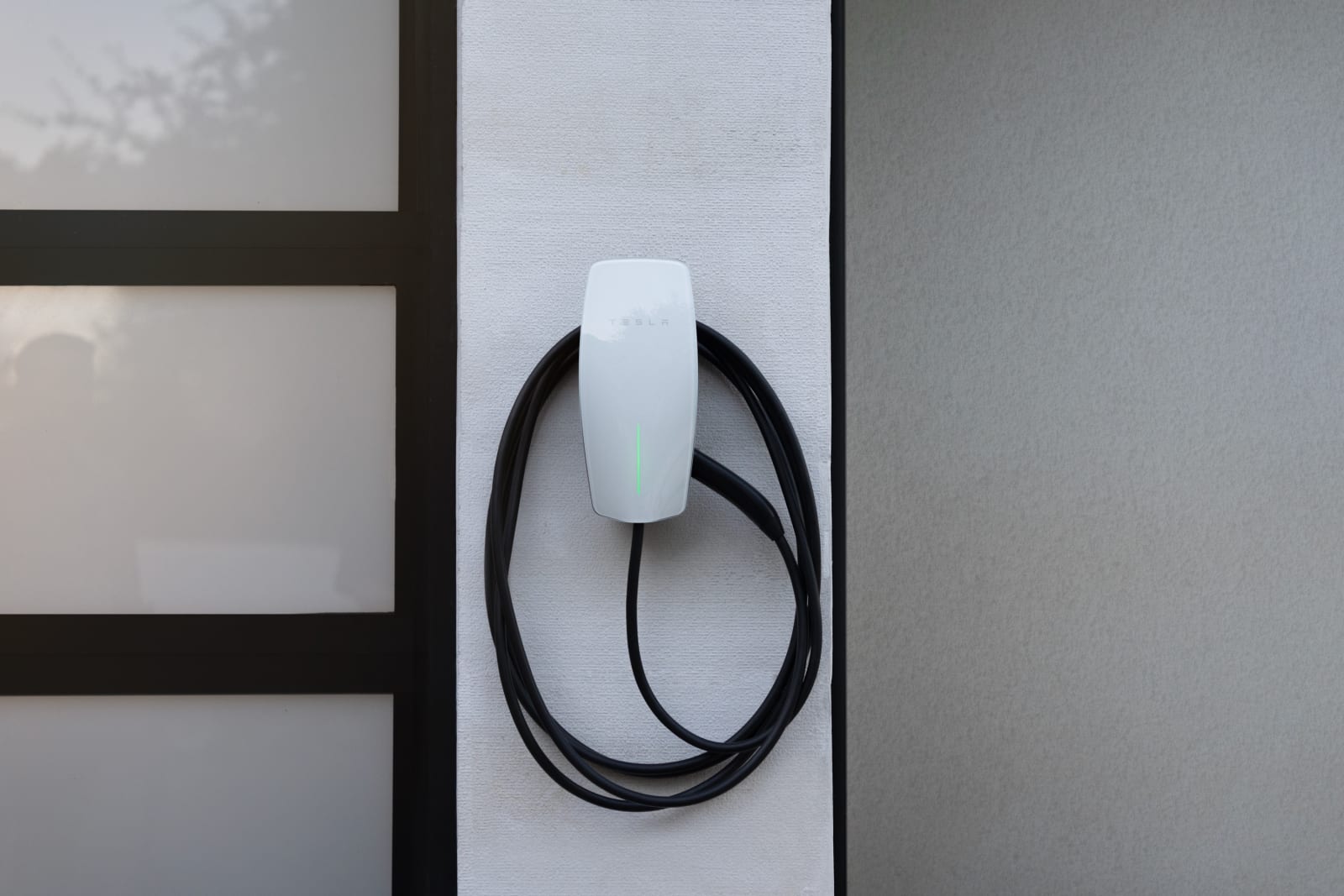 Close up of a Tesla Wall Connector charger mounted on a white wall with the charging cable neatly coiled.