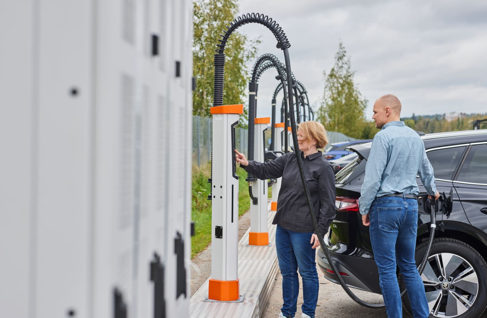A driver plugging into a Kempower satellite charger at a public charging site