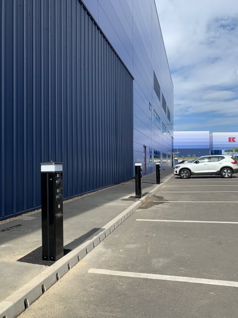 Row of Rolec EV charging pedestals along the warehouse wall with vehicle charging at Zeus Packaging, Biggleswade.