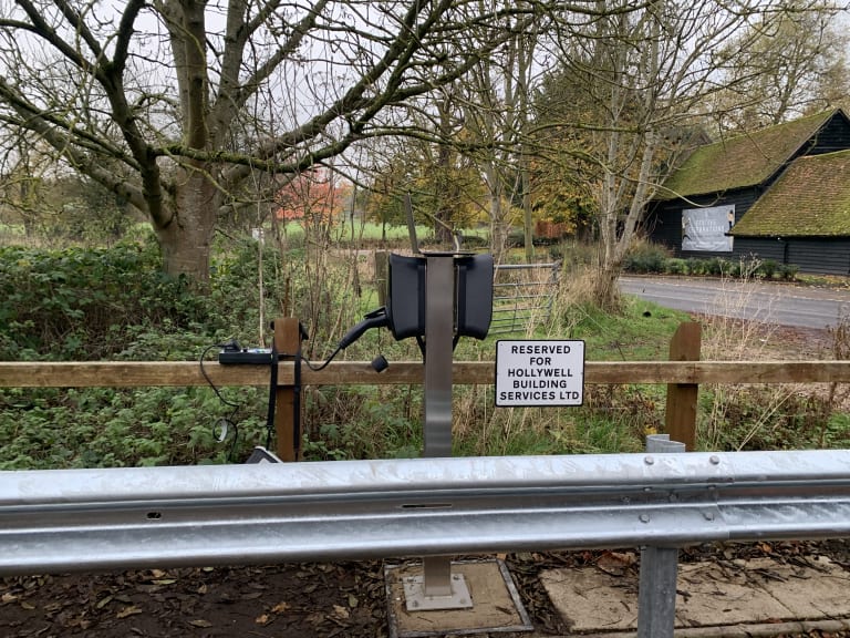 A dual EO Genius 2 charging pedestal with crash barrier and reserved bay sign at Hollywell's fleet depot in St Albans.