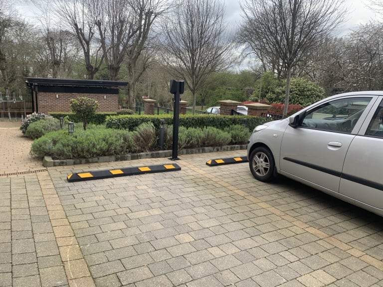 A black EV charging pedestal installed in a parking bay with safety wheel stops at a residential car park in Hendon.