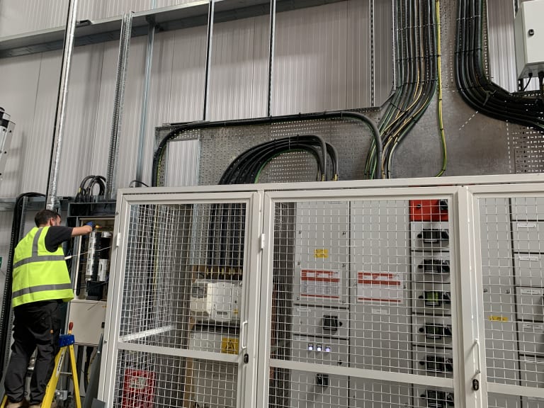 Electrician connecting EV charging circuits at the main distribution board inside Zeus Packaging facility, Biggleswade