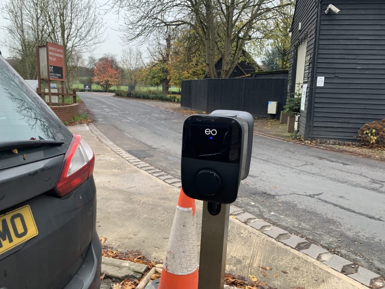 An EO Genius pedestal charger with a blue status light in a UK office car park.