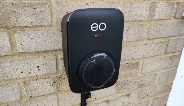 An EO Mini Pro 3 home charger showing a red fault light, mounted on a brick wall at a UK home.