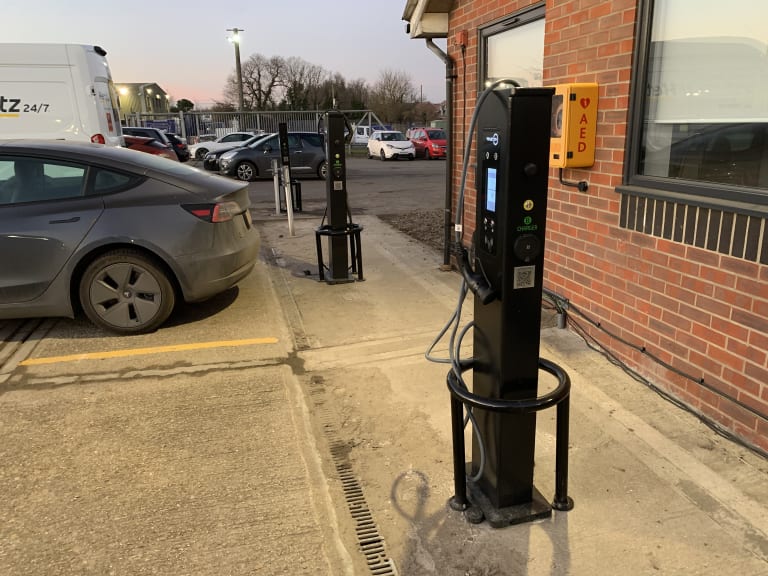 Two freestanding pedestal EV chargers installed in a commercial car park beside an office building in the UK.