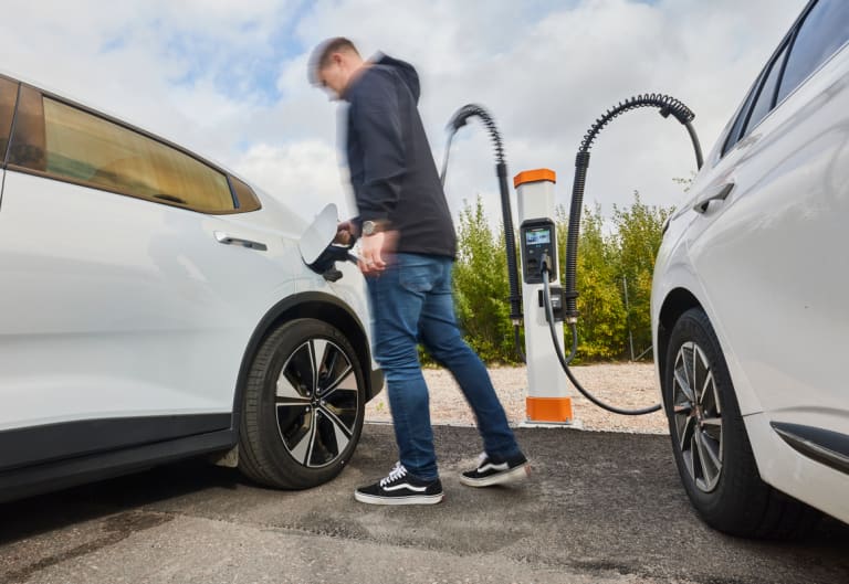 Driver plugging in an electric vehicle between two white cars at a Kempower dual charging point.