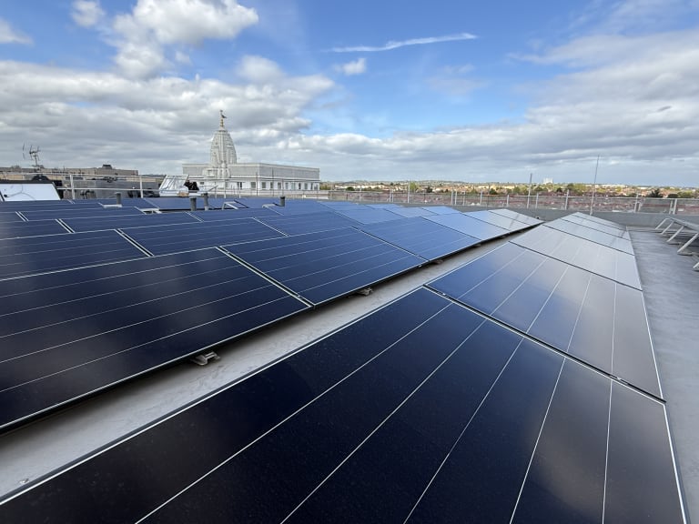 Ballasted black framed solar panels across a flat commercial rooftop at Alpine Place, Colindale, with Neasden temple on the London horizon