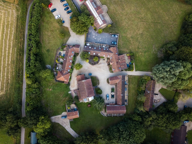 Aerial view of a cluster of holiday cottages and their car park in the Devon countryside.