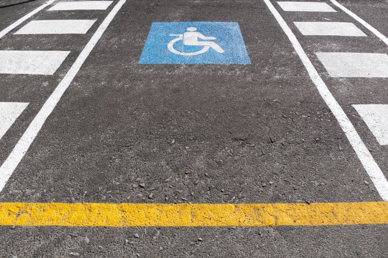 A blue wheelchair accessibility symbol painted in a marked disabled parking bay with hatched access markings.