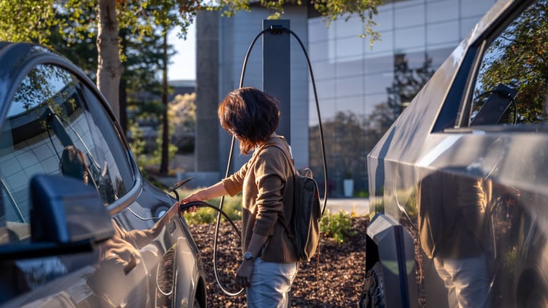 A guest walks toward a car connected to a Tesla Destination Charging point in a business car park.