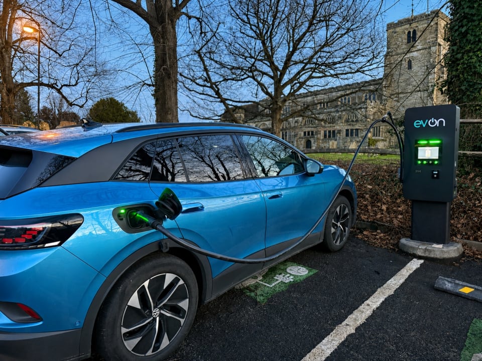 An evon pedestal EV charger illuminated at dusk in a car park